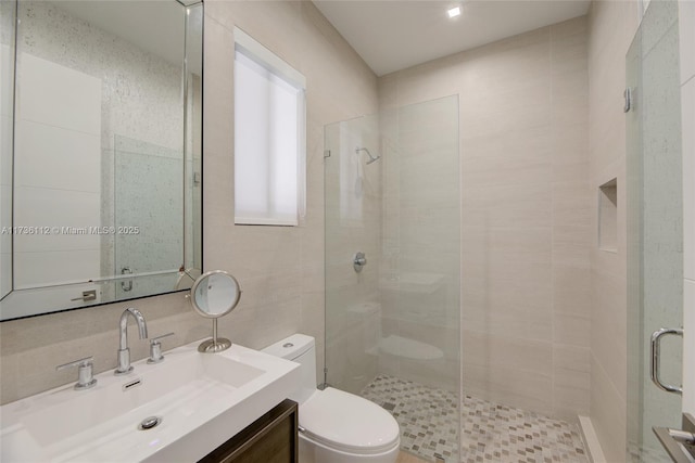 bathroom featuring tile walls, toilet, a stall shower, and vanity