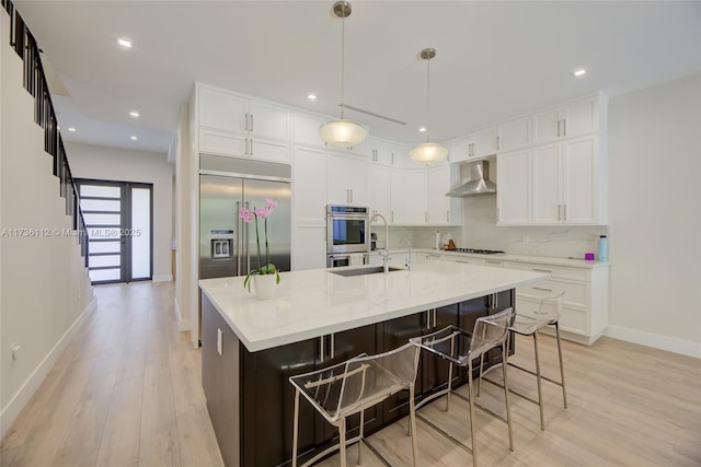 kitchen featuring a breakfast bar, tasteful backsplash, a large island with sink, light stone countertops, and wall chimney range hood