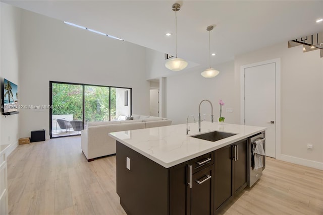 kitchen with pendant lighting, sink, a kitchen island with sink, light stone countertops, and light wood-type flooring