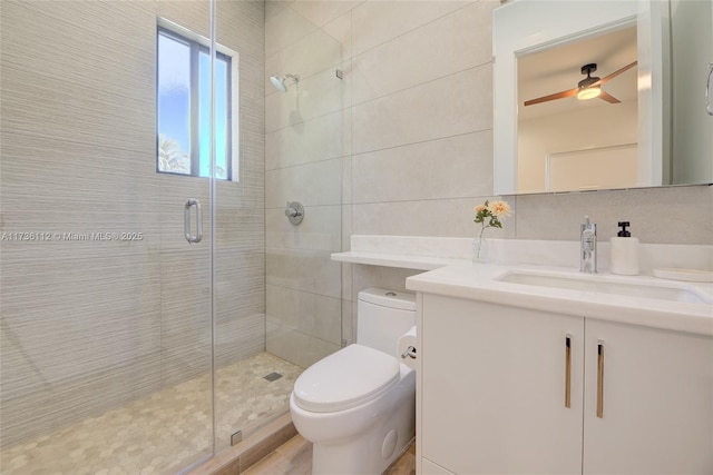 bathroom featuring toilet, vanity, a shower stall, ceiling fan, and tile walls