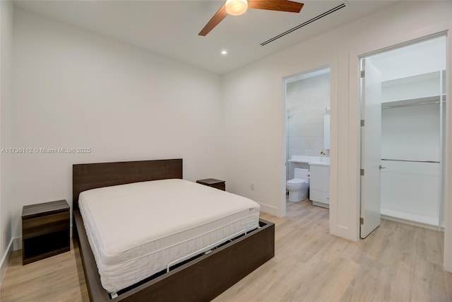 bedroom featuring connected bathroom, a spacious closet, light hardwood / wood-style floors, and ceiling fan