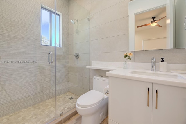 bathroom with ceiling fan, tile walls, vanity, toilet, and walk in shower