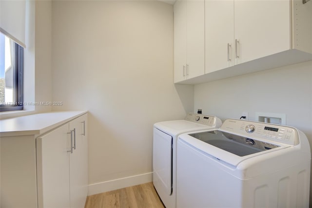 laundry area with cabinets, washing machine and dryer, and light hardwood / wood-style floors