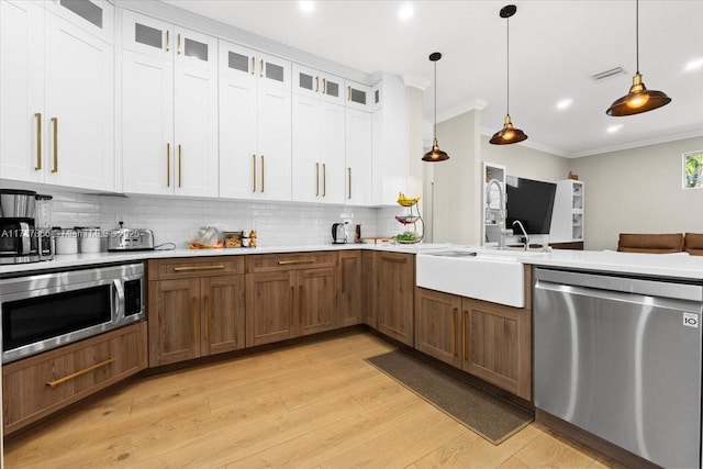 kitchen with appliances with stainless steel finishes, white cabinetry, backsplash, hanging light fixtures, and ornamental molding