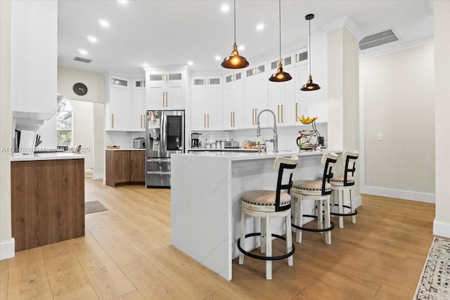 kitchen with stainless steel fridge with ice dispenser, light wood-type flooring, ornamental molding, pendant lighting, and white cabinets