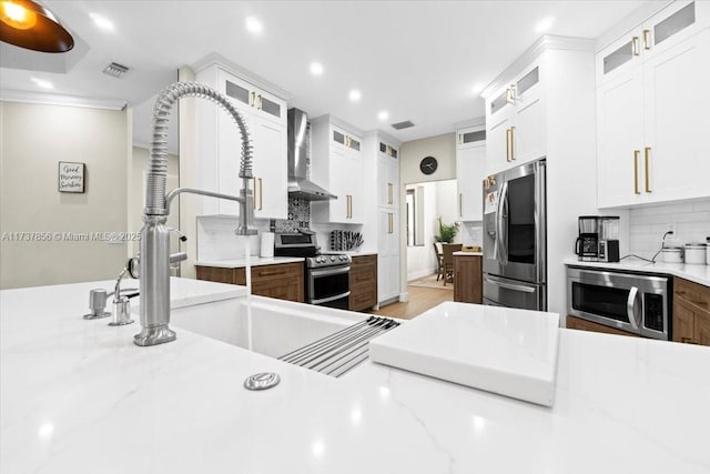 kitchen with stainless steel appliances, white cabinetry, wall chimney range hood, and light stone counters