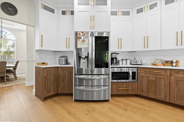 kitchen with appliances with stainless steel finishes, light hardwood / wood-style flooring, white cabinets, and decorative backsplash