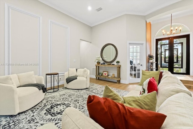 living room with french doors, crown molding, an inviting chandelier, and light hardwood / wood-style flooring