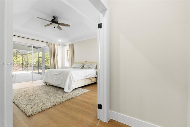 bedroom with crown molding, hardwood / wood-style flooring, ceiling fan, access to exterior, and a tray ceiling