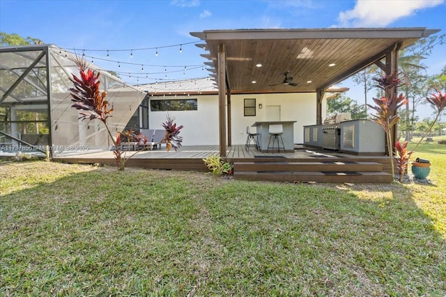 rear view of house featuring a lawn, a wooden deck, an outdoor kitchen, a lanai, and ceiling fan