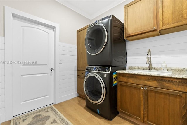 clothes washing area featuring sink, cabinets, stacked washer and clothes dryer, crown molding, and light wood-type flooring