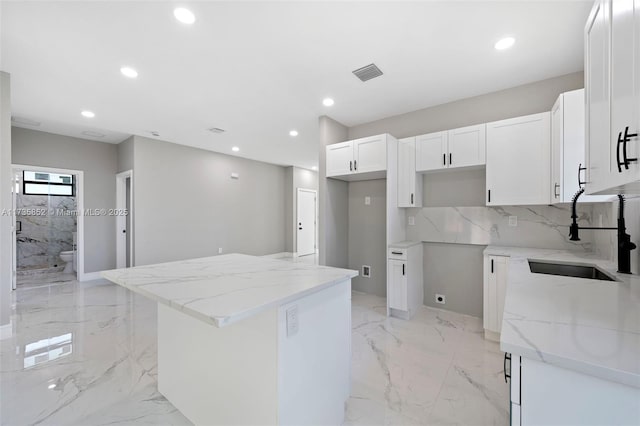 kitchen featuring white cabinetry, a center island, sink, and light stone counters