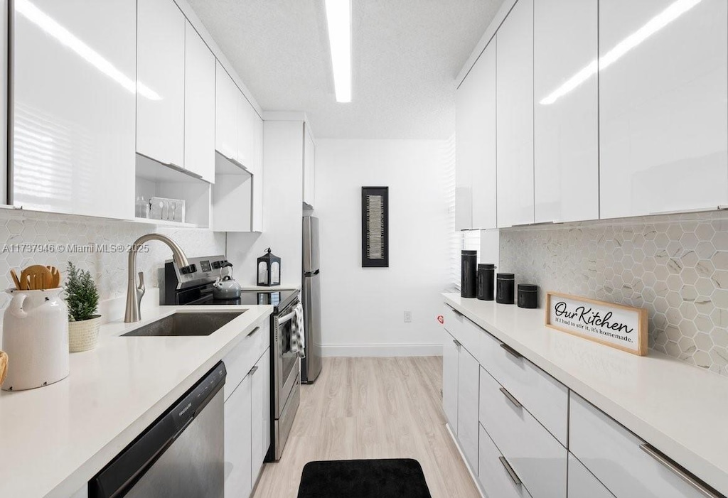 kitchen with appliances with stainless steel finishes, sink, white cabinets, and backsplash