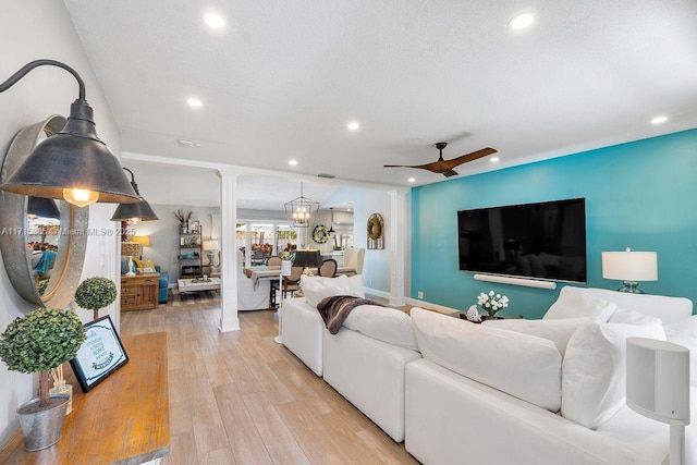 living room with ceiling fan, light hardwood / wood-style floors, a textured ceiling, and ornate columns