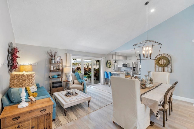 dining space featuring an inviting chandelier, vaulted ceiling, and light wood-type flooring