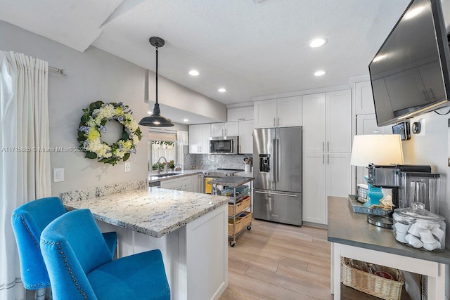 kitchen featuring appliances with stainless steel finishes, decorative light fixtures, white cabinets, kitchen peninsula, and light wood-type flooring