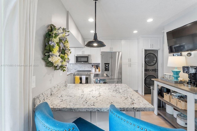 kitchen with appliances with stainless steel finishes, pendant lighting, tasteful backsplash, white cabinets, and stacked washer / drying machine