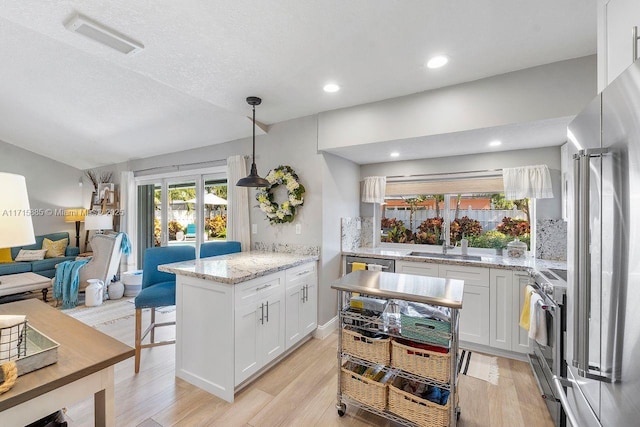 kitchen featuring light stone counters, decorative light fixtures, high quality appliances, a kitchen island, and white cabinets