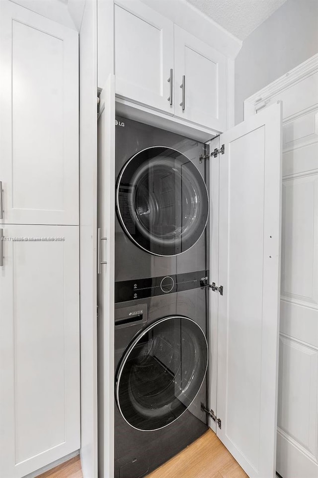 laundry area with stacked washer and dryer, light hardwood / wood-style flooring, and a textured ceiling