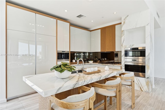 kitchen featuring white cabinetry, appliances with stainless steel finishes, a kitchen island with sink, and light stone counters