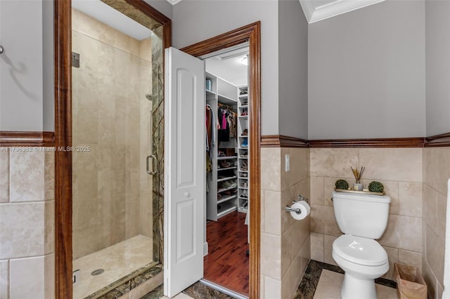 bathroom with tile walls, crown molding, a shower with door, and toilet