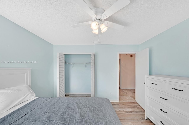 unfurnished bedroom featuring ceiling fan, a textured ceiling, light hardwood / wood-style floors, and a closet