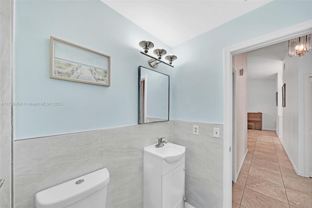 bathroom featuring tile patterned flooring, tile walls, vanity, vaulted ceiling, and toilet