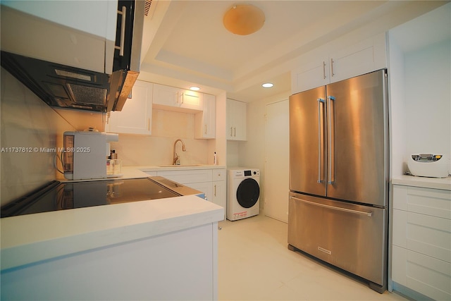 kitchen with high quality fridge, washer / clothes dryer, white cabinetry, sink, and a tray ceiling