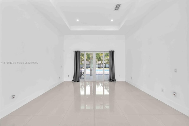 unfurnished room featuring light tile patterned flooring, a tray ceiling, and a high ceiling