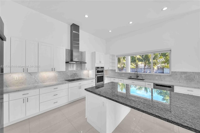 kitchen featuring wall chimney range hood, appliances with stainless steel finishes, light stone counters, white cabinets, and backsplash