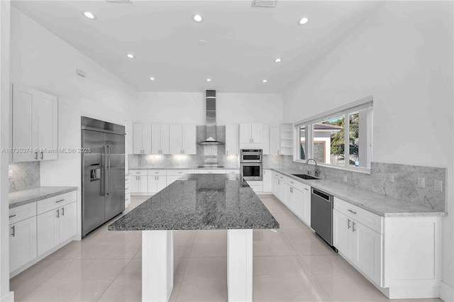 kitchen with appliances with stainless steel finishes, wall chimney range hood, a kitchen island, recessed lighting, and tasteful backsplash