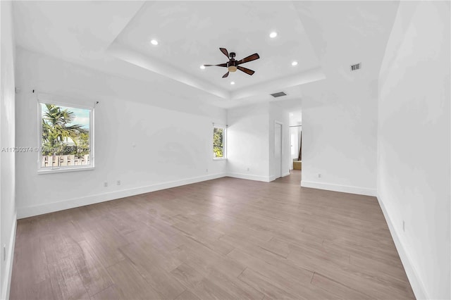 unfurnished room featuring a raised ceiling, plenty of natural light, recessed lighting, a ceiling fan, and wood finished floors