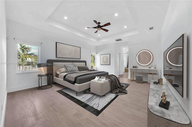 bedroom with recessed lighting, multiple windows, a tray ceiling, wood finished floors, and a ceiling fan