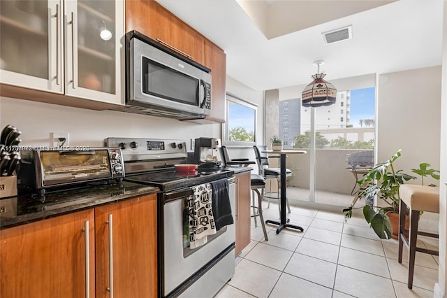 kitchen with visible vents, glass insert cabinets, brown cabinets, dark stone countertops, and stainless steel appliances