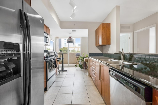 kitchen with light tile patterned flooring, stainless steel appliances, a sink, visible vents, and brown cabinetry