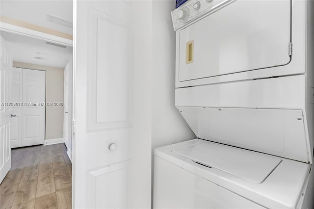 clothes washing area with stacked washer and dryer, visible vents, laundry area, and light wood-style floors