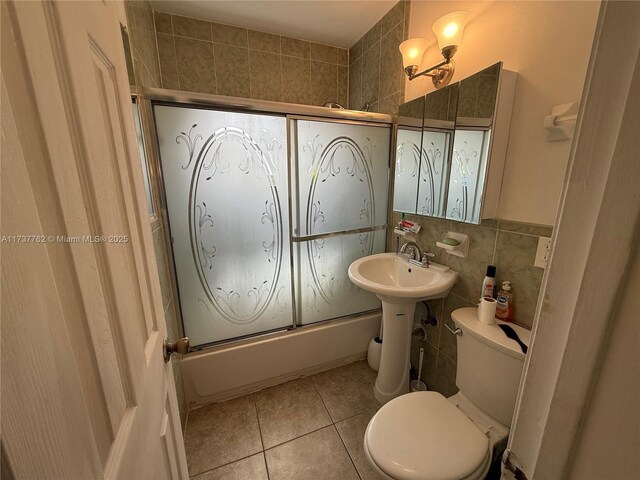 full bathroom featuring tile patterned floors, toilet, sink, bath / shower combo with glass door, and tile walls