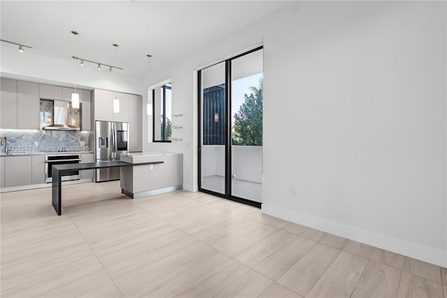 kitchen with appliances with stainless steel finishes, tasteful backsplash, white cabinetry, hanging light fixtures, and wall chimney exhaust hood