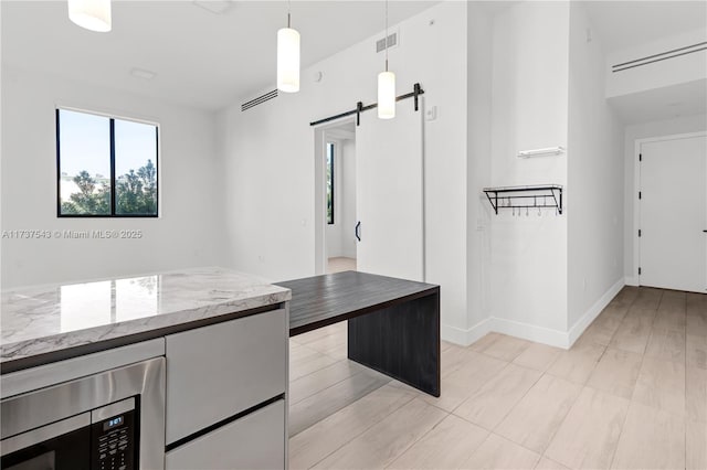 kitchen featuring stainless steel microwave, hanging light fixtures, a barn door, and butcher block counters