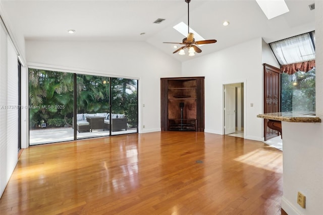 unfurnished living room with high vaulted ceiling, a skylight, light hardwood / wood-style floors, and ceiling fan