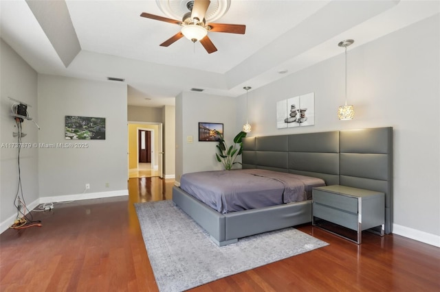 bedroom with ceiling fan, dark hardwood / wood-style flooring, and a tray ceiling