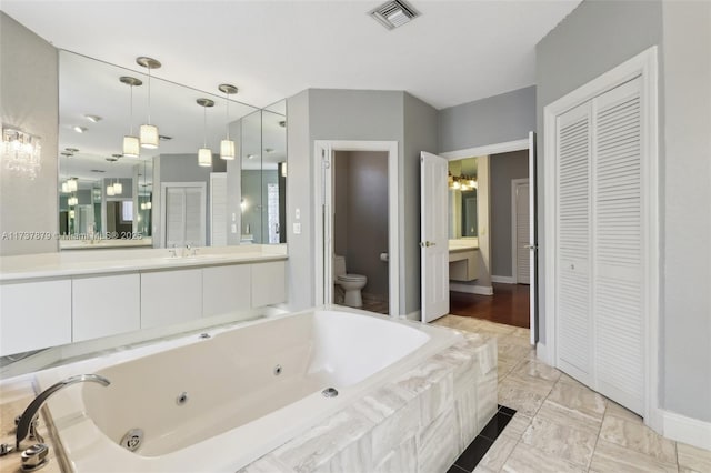 bathroom featuring vanity, toilet, and tiled bath