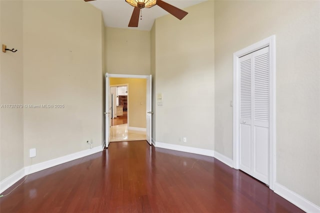 unfurnished bedroom with dark hardwood / wood-style flooring, a towering ceiling, a closet, and ceiling fan