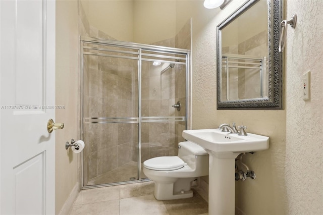 bathroom with tile patterned flooring, sink, a shower with shower door, and toilet