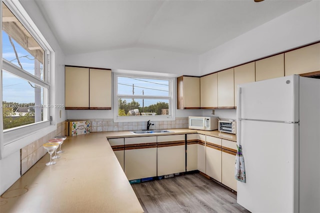 kitchen featuring vaulted ceiling, cream cabinets, sink, and white appliances