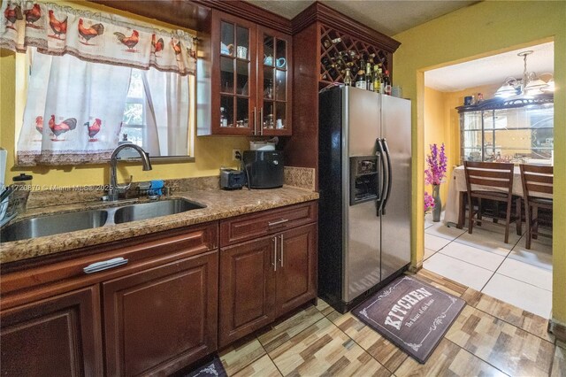 kitchen with stainless steel refrigerator with ice dispenser, sink, an inviting chandelier, decorative light fixtures, and light stone countertops