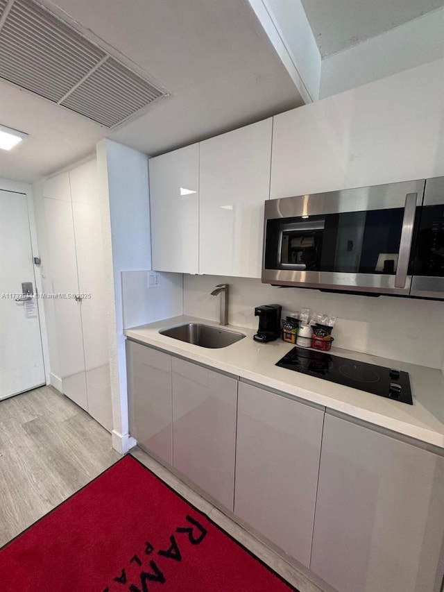 kitchen featuring white cabinetry, black electric cooktop, sink, and light hardwood / wood-style floors