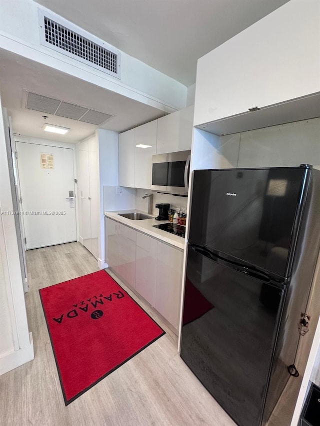 kitchen featuring white cabinetry, sink, light wood-type flooring, and black appliances