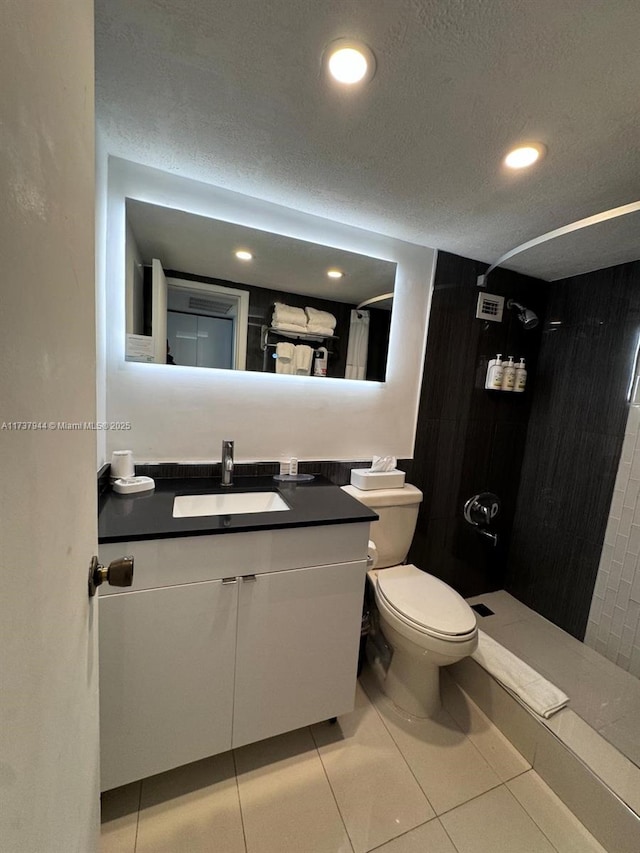 bathroom featuring a tile shower, vanity, a textured ceiling, tile patterned floors, and toilet