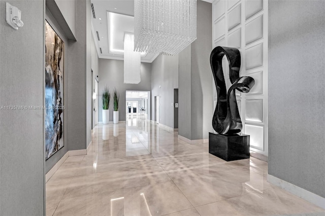 corridor featuring a towering ceiling, a notable chandelier, and a tray ceiling